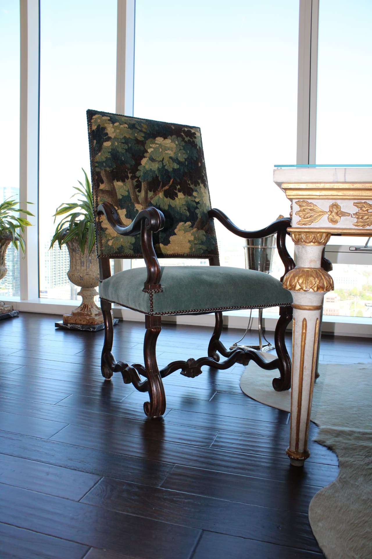 Carved walnut armchair with a verdure tapestry back and moss-green velvet seat beside a gilded console — Downtown Nashville, Nashville